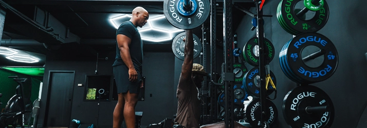 Mo May watching a person lift weights.